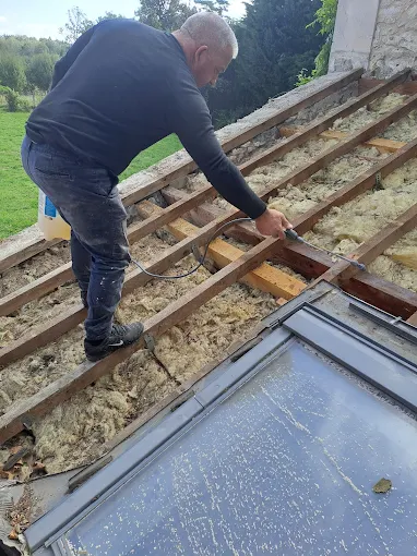 Couvreur de FM Couverture 77 intervenant sur l’isolation et la structure de toiture autour d’une fenêtre de toit avec charpente apparente