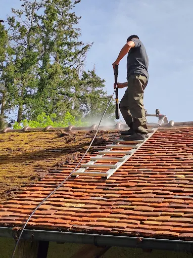 Couvreur de FM Couverture 77 réalisant le nettoyage d’une toiture en tuiles à l’aide d’un nettoyeur haute pression avec échelle d’accès